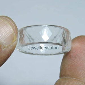 Può includere: Un anello di vetro trasparente con un design sfaccettato. L'anello è tenuto tra due dita. Il testo "JewellerySafari" è visibile all'interno dell'anello.