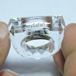 Puede incluir: Un anillo de cristal transparente con un dise&ntilde;o facetado. El anillo se sostiene en una mano.