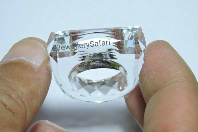 Puede incluir: Un anillo de cristal transparente con un dise&ntilde;o facetado. El anillo se sostiene en una mano.