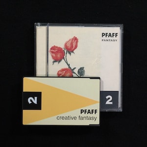 Op de afbeelding: Twee plastic koffers voor een Pfaff naaimachine borduurontwerp. De bovenste koffer heeft een witte achtergrond met een rood rozenontwerp en de tekst "Pfaff Fantasy". De onderste koffer heeft een gele achtergrond met de tekst "Pfaff creative fantasy" en het nummer "2" aan beide kanten.