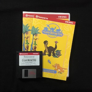 Könnte beinhalten: Vintage Stickmuster-Set mit dem Thema "In einem Land vor unserer Zeit". Das Set enthält eine 3,5-Zoll-Diskette und zwei gelbe Broschüren mit Dinosaurier-Illustrationen. Die Logos Husqvarna und Viking sind sichtbar.