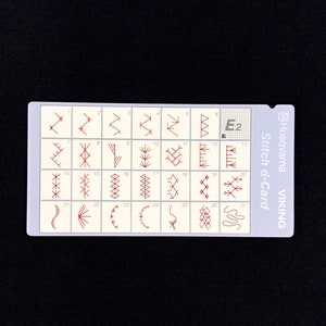 Puede incluir: Una tarjeta rectangular blanca Husqvarna Viking Stitch d-Card E2 que presenta una cuadrícula de veintisiete patrones de puntadas de bordado rojos numerados secuencialmente. La tarjeta incluye el nombre de la marca y el modelo en gris.