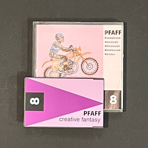 Puede incluir: Una cinta de casete rosa y morada con el texto "PFAFF creative fantasy" y el número "8" en la parte delantera. La cinta de casete está en una caja de plástico transparente con una imagen de una persona conduciendo una motocicleta.