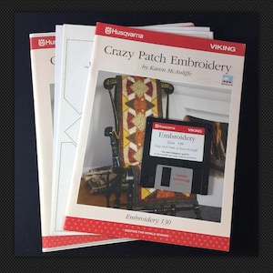 Puede incluir: Una pila de tres libros titulada "Crazy Patch Embroidery" de Karen McAuliffe. El libro es para una máquina de bordar Viking e incluye un disquete etiquetado como "Embroidery Disk 130".