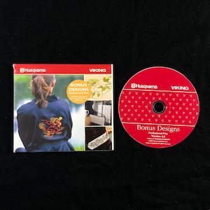 Puede incluir: Un CD rojo con el texto "Bonus Designs Professional Plus Version 6.0" y los logotipos de Husqvarna y Viking. El CD viene empaquetado con un folleto que muestra a una mujer con una chaqueta negra con un diseño bordado.