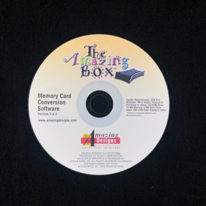 May include: A silver CD-ROM disc with a yellow and orange label. The label says "The Amazing Box" and "Memory Card Conversion Software Version 3.6.2" with the website address "www.amazingdesigns.com".