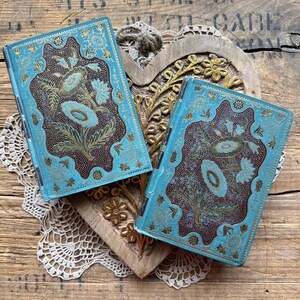 May include: Two vintage blue and gold journals with intricate floral designs. The journals are resting on a wooden heart-shaped surface.