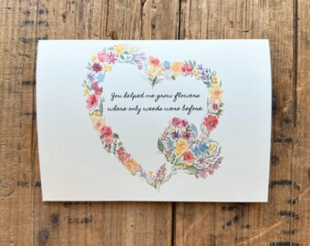 May include: A card with a watercolor illustration of a heart made of flowers. The text reads "You helped me grow flowers where only weeds were before."
