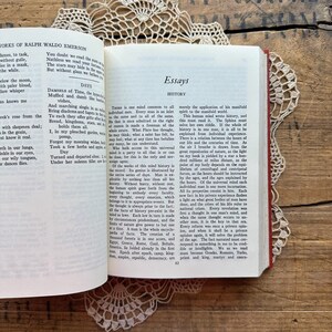 May include: A close-up of a book with a red cover and gold lettering. The title of the book is "Essays" and the author is Ralph Waldo Emerson. The text on the page discusses the concept of history as a reflection of the universal mind.