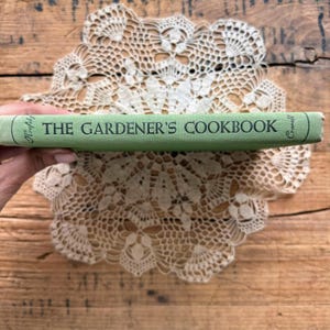May include: A light green hardcover book spine titled THE GARDENER'S COOKBOOK in dark green lettering. The author names Krofsky and Crowell are printed on the left and right ends of the spine respectively, featuring a clean, simple design.