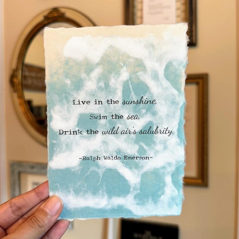 Pode incluir: Um cart&atilde;o de papel marmorizado azul e branco com a cita&ccedil;&atilde;o "Viva sob o sol, nade no mar, beba a salubridade do ar selvagem -Ralph Waldo Emerson-"
