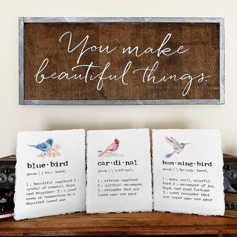 May include: Three framed prints with watercolor illustrations of a bluebird, cardinal, and hummingbird. Each print includes the bird's name and a definition of its symbolism. The top sign reads "You make beautiful things."