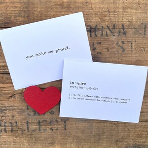 May include: A white card with the text "you make me proud."  A second white card with the text "inspire" and its definition. A red felt heart is placed on the cards.