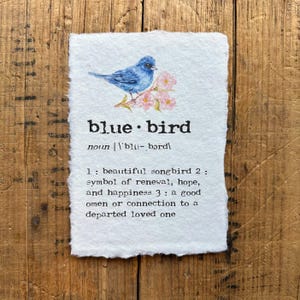 May include: A watercolor illustration of a bluebird perched on a branch with pink flowers. The image is accompanied by a definition of the word "bluebird" as a noun, with the pronunciation and three meanings.