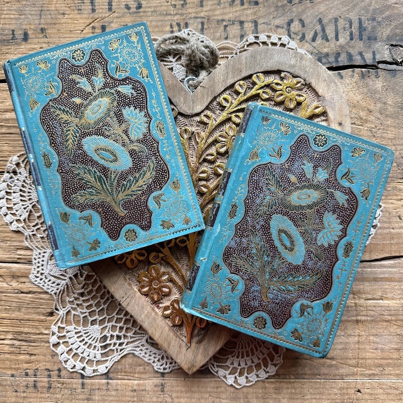 May include: Two vintage blue and gold journals with intricate floral designs. The journals are resting on a wooden heart-shaped surface.