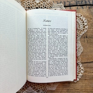 May include: A vintage book with a red cover and gold lettering. The title of the book is "Nature" and the text on the page discusses the concept of nature and its relationship to humanity.