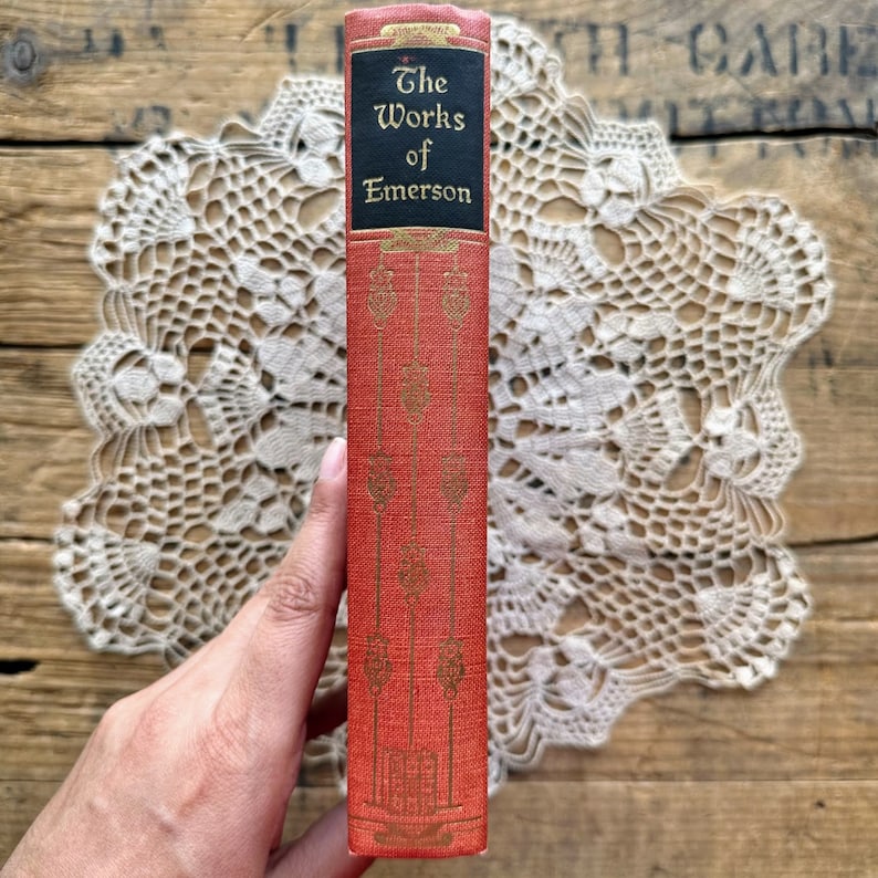 May include: A red hardcover book with gold lettering on the spine. The title is "The Works of Emerson".