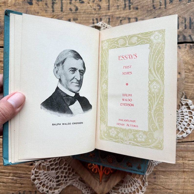 May include: A vintage book titled "Essays: First Series" by Ralph Waldo Emerson, published by Henry Altemus in Philadelphia. The cover features a portrait of Emerson and an ornate floral design.