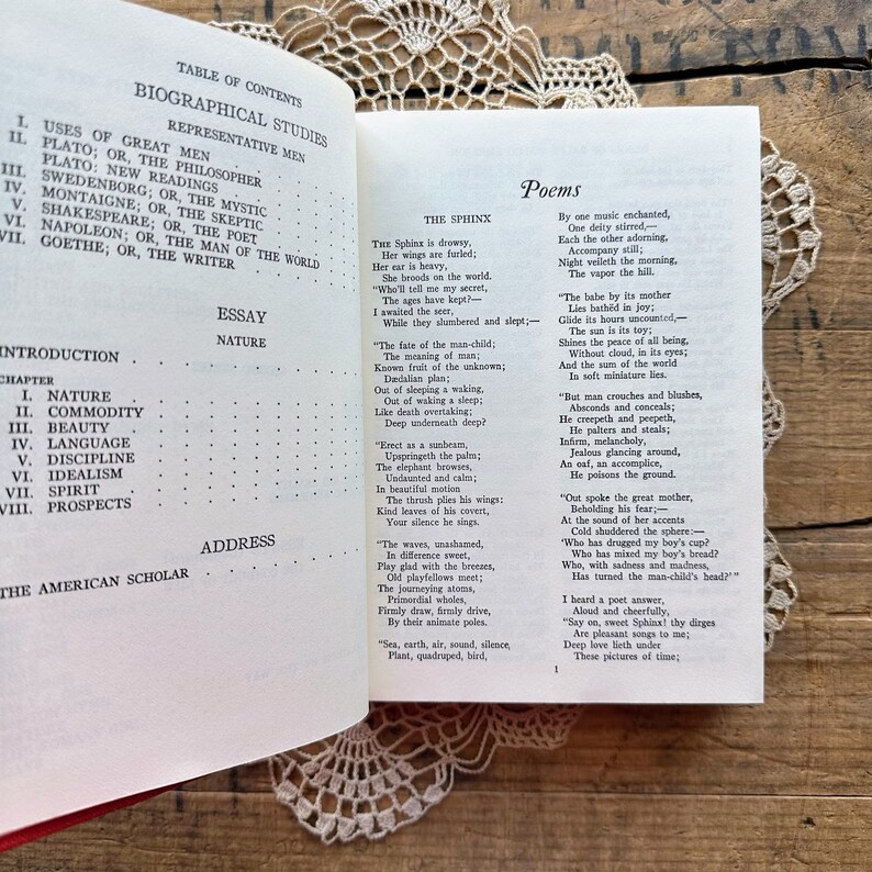 May include: An open book with a red cover and white pages. The book is titled "Biographical Studies" and includes a table of contents with chapters on Plato, Swedenborg, Montaigne, Shakespeare, Napoleon, and Goethe. The book also includes an essay on nature and a section of poems.