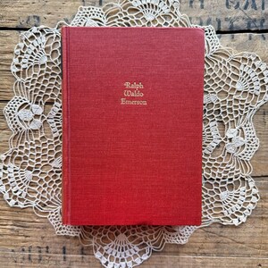 May include: A red hardcover book with the title "Ralph Waldo Emerson" printed in gold lettering on the front cover.