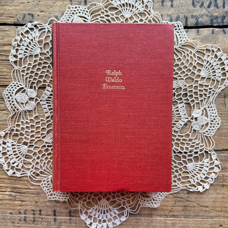 May include: A red hardcover book with the title "Ralph Waldo Emerson" printed in gold lettering on the front cover.