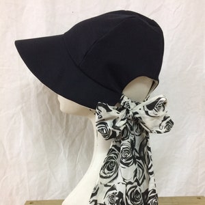 Könnte beinhalten: Ein schwarzer Sonnenhut mit breiter Krempe und einem schwarz-weißen Rosenmusterband, das hinten gebunden ist.