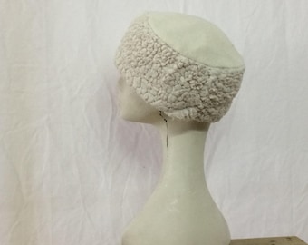 Puede incluir: Un gorro blanco de piel sintética con una corona redonda y un ala ancha. El gorro está hecho de un material suave y esponjoso y tiene un diseño simple y clásico.