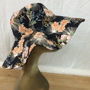 May include: A wide-brimmed sun hat with a black background and a floral print featuring pink, orange, and yellow flowers. The hat has a wide brim that curves down on the sides.