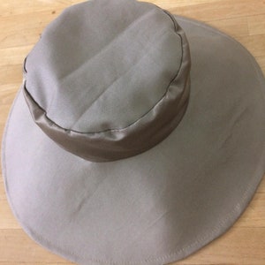 May include: A wide-brimmed sun hat in a light beige color with a matching fabric band around the crown.