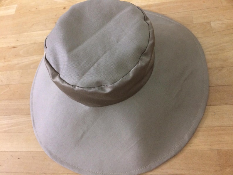 May include: A wide-brimmed sun hat in a light beige color with a matching fabric band around the crown.