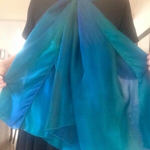 May include: A blue and green ombre silk scarf tied around the neck in a loose knot.