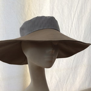 May include: A wide-brimmed sun hat with a tan colored crown and a black and white striped band around the base of the crown.