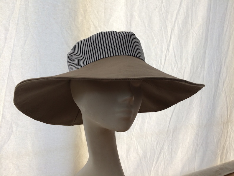 May include: A wide-brimmed sun hat with a tan colored crown and a black and white striped band around the base of the crown.