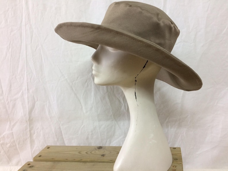 May include: A wide-brimmed, tan-colored sun hat with a slightly rounded crown. The hat is made of a soft, pliable material and has a simple, classic design.