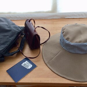May include: A brown leather purse, a black leather handbag, a blue passport, and a tan sun hat with a black and white striped band.