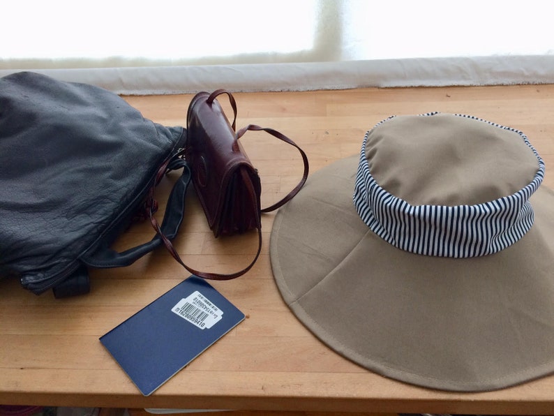 May include: A brown leather purse, a black leather handbag, a blue passport, and a tan sun hat with a black and white striped band.