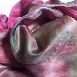 May include: A soft, sheer fabric scarf in shades of pink, green, and brown. The fabric is gathered and draped, showing its flowing texture.