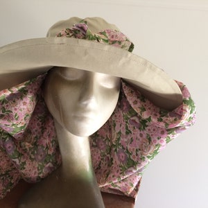 Op de afbeelding: Een brede zonnehoed met een bloemenprint nekflap. De hoed is beige en de stof is roze en groen.