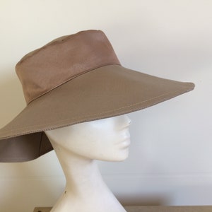 May include: A wide-brimmed sun hat in a light brown color. The hat has a slightly rounded crown and a wide, flat brim that extends out from the crown.