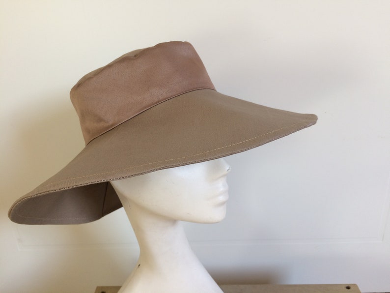 May include: A wide-brimmed sun hat in a light brown color. The hat has a slightly rounded crown and a wide, flat brim that extends out from the crown.