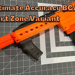 Op de afbeelding: Een oranje en zwart speelgoedpistool met de tekst "Ultimate Accuracy BCAR Dart Zone Variant" erop gedrukt. Het pistool ligt op een zwart-wit raster.