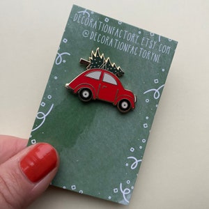 Könnte beinhalten: Rote Emaille-Anstecknadel mit einem Oldtimer, auf dem ein Weihnachtsbaum liegt. Die Anstecknadel befindet sich auf einer grünen Karte mit weißen Punkten und dem Text "decorationfactory.etsy.com @decorationfactorynl".