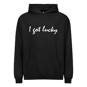 May include: Black hooded sweatshirt with a front pocket and white text that reads "I got lucky". The hoodie has a drawstring and a hood. The sweatshirt is made of a soft material.