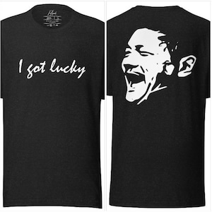 May include: Black t-shirt with white text that says "I got lucky" on the front and a white silhouette of a person laughing on the back.