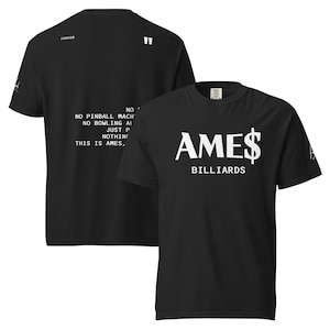 May include: Black t-shirt with the text "AMES BILLIARDS" in white. The front of the shirt features the word "AMES" with a dollar sign, and "BILLIARDS" below. The back of the shirt has text that reads "NO PINBALL MACH, NO BOWLING AI, JUST P, NOTHING, THIS IS AMES,"