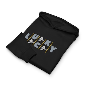 May include: Black hoodie with the word "LUCKY" in gray letters. The letter "U" and "C" have a graphic of a face with a surprised expression. The hoodie has a hood and long sleeves.