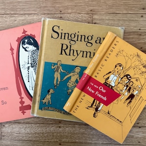 May include: Three vintage children's books are displayed on a wooden surface. The books are titled "Seven or So", "Singing and Rhyming", and "The New Our New Friends". The covers feature illustrations and text in various colors.