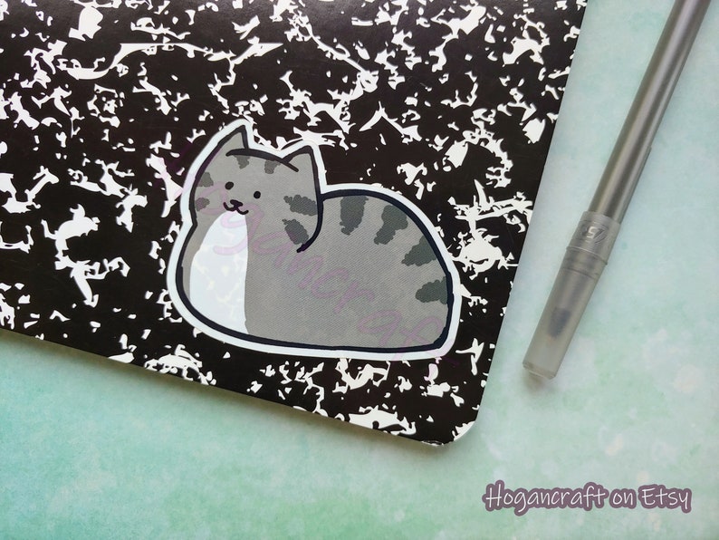 Puede incluir: Una pegatina de gato de dibujos animados gris y blanco sobre un fondo moteado en blanco y negro. La pegatina es de un gato acostado de lado con las patas metidas debajo del cuerpo.