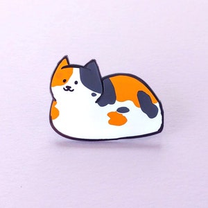 May include: A black, orange, and white enamel pin of a cartoon cat lying on its side.