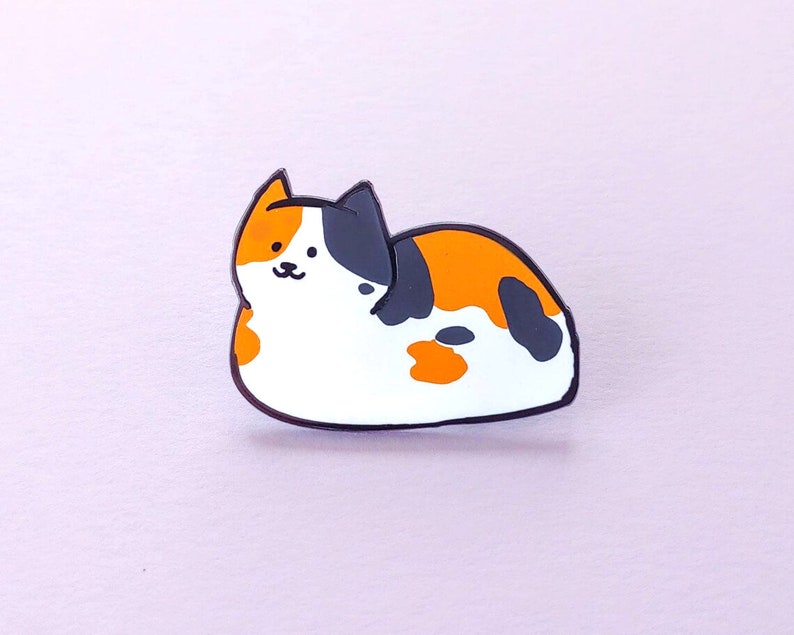 May include: A black, orange, and white enamel pin of a cartoon cat lying on its side.